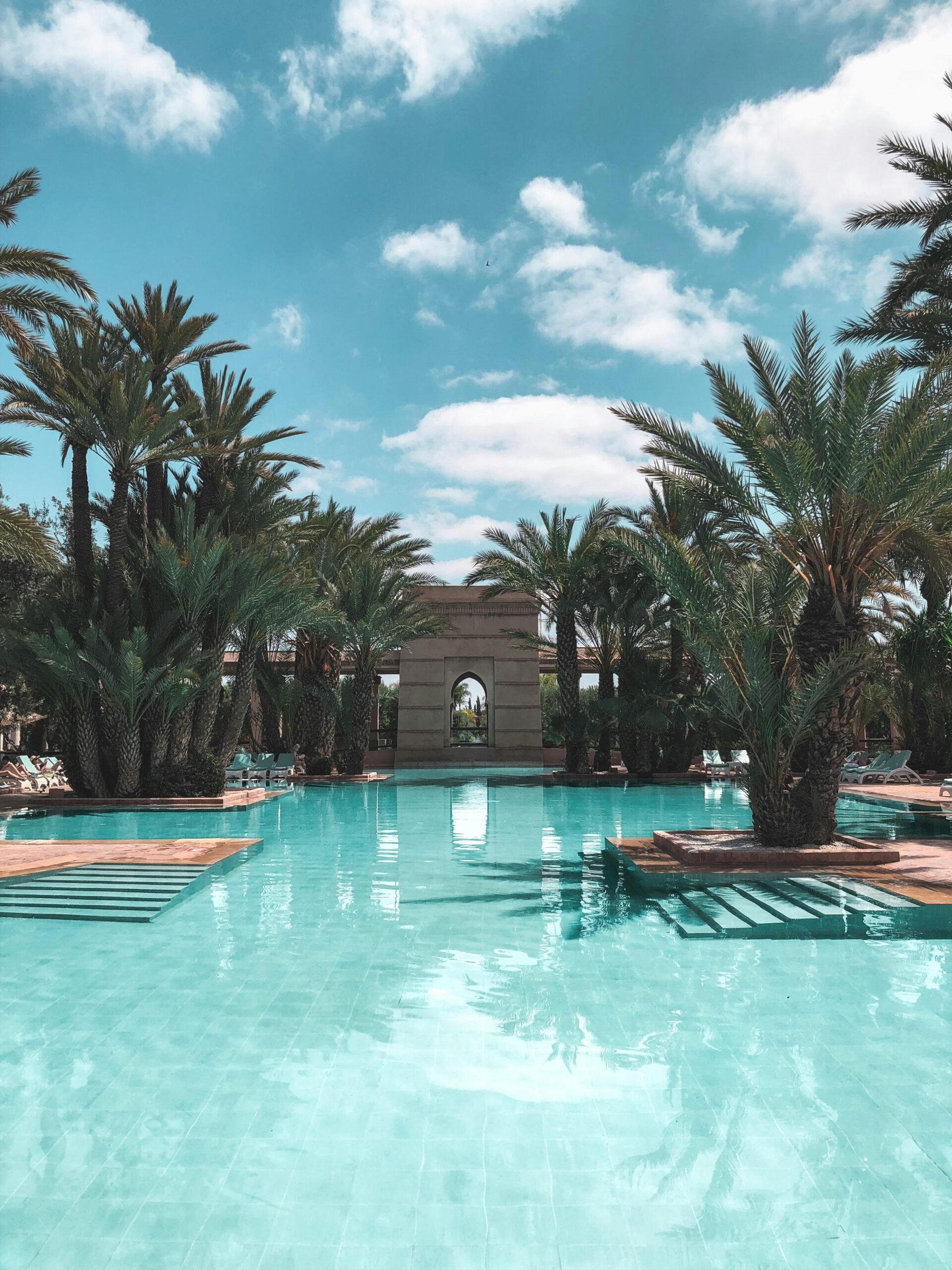 Discover tranquility at this serene pool surrounded by lush palm trees under a bright blue sky in Marrakech.